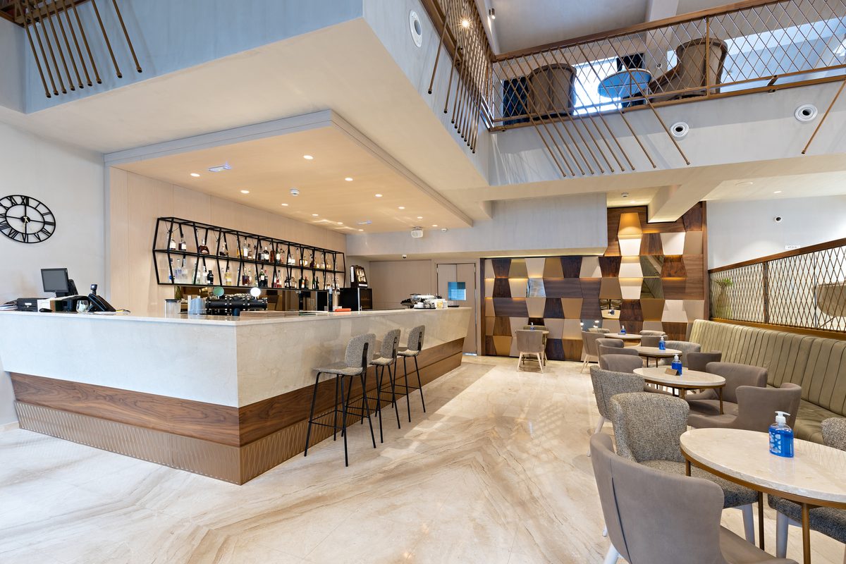 A cafe counter with bar stools and lounge seating under a double-height atrium with recessed downlights