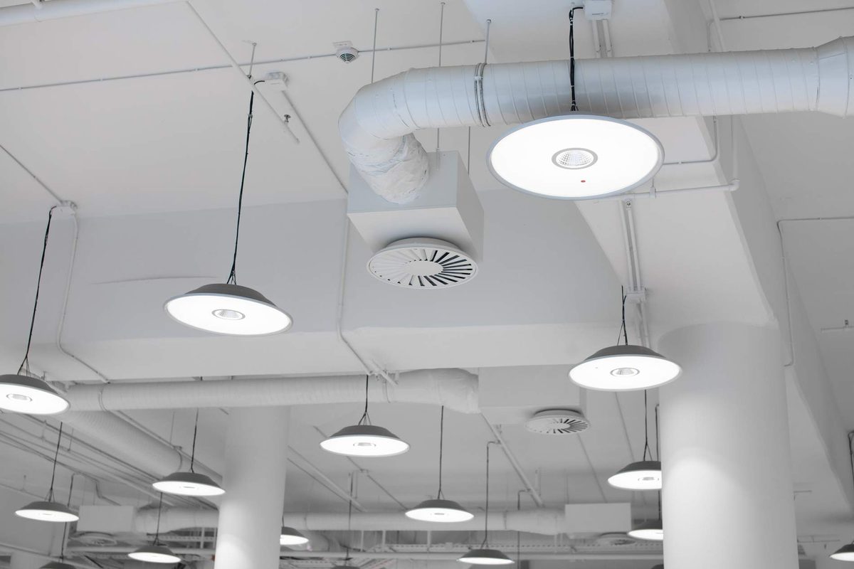 White pendant lights hanging from an exposed ceiling with ventilation ducting