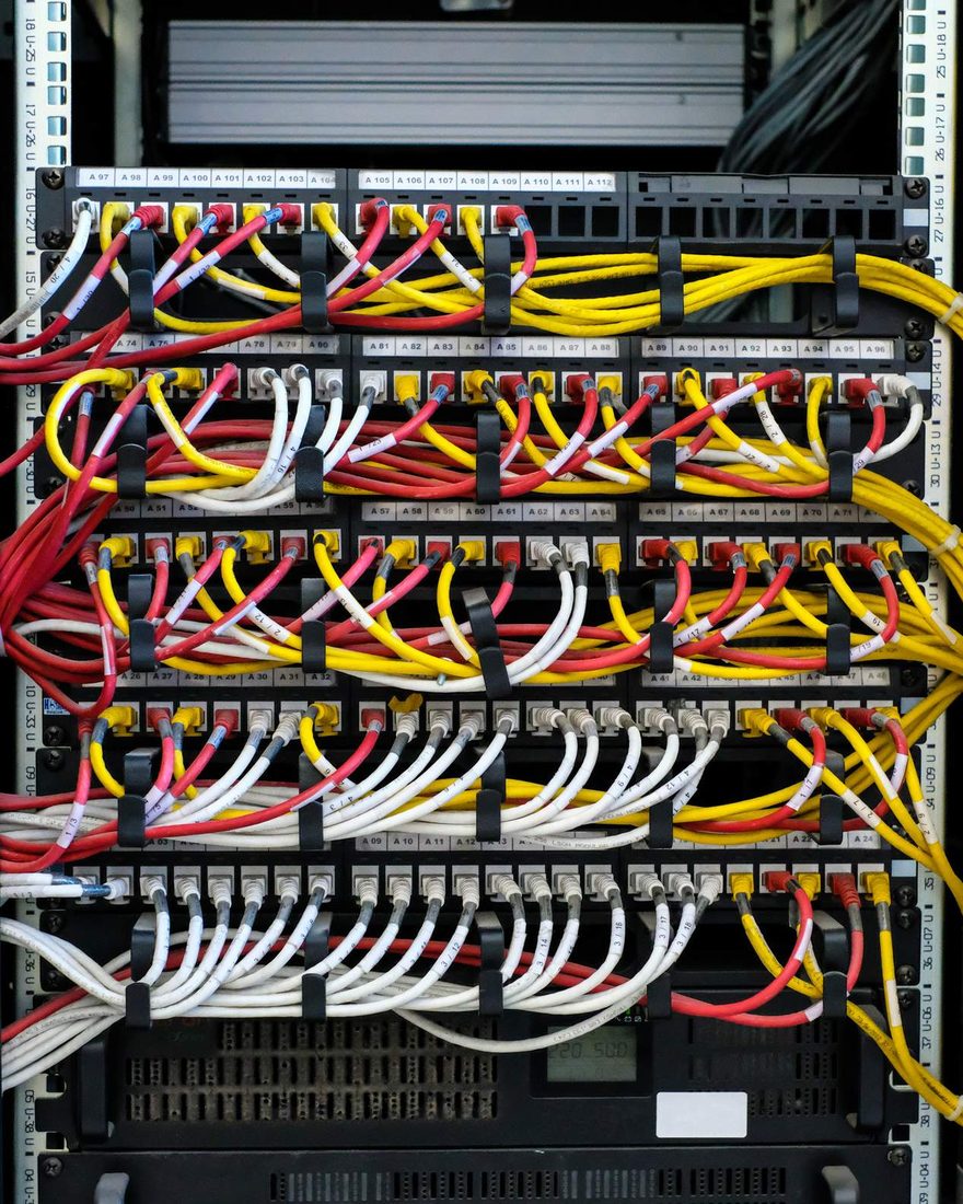 A data cabinet with rows of patch panels and red, yellow and white network cables