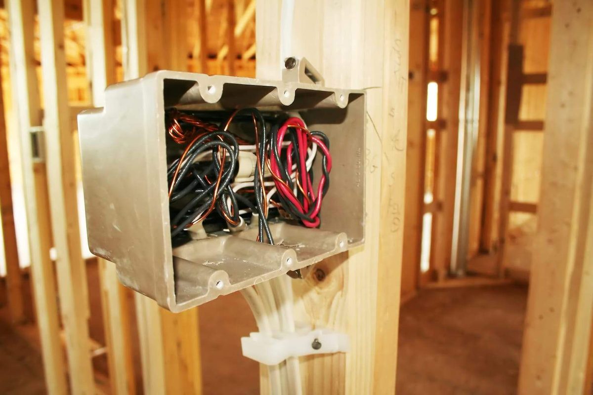 An electrical box with red and black wires fixed to timber framing in a house under construction